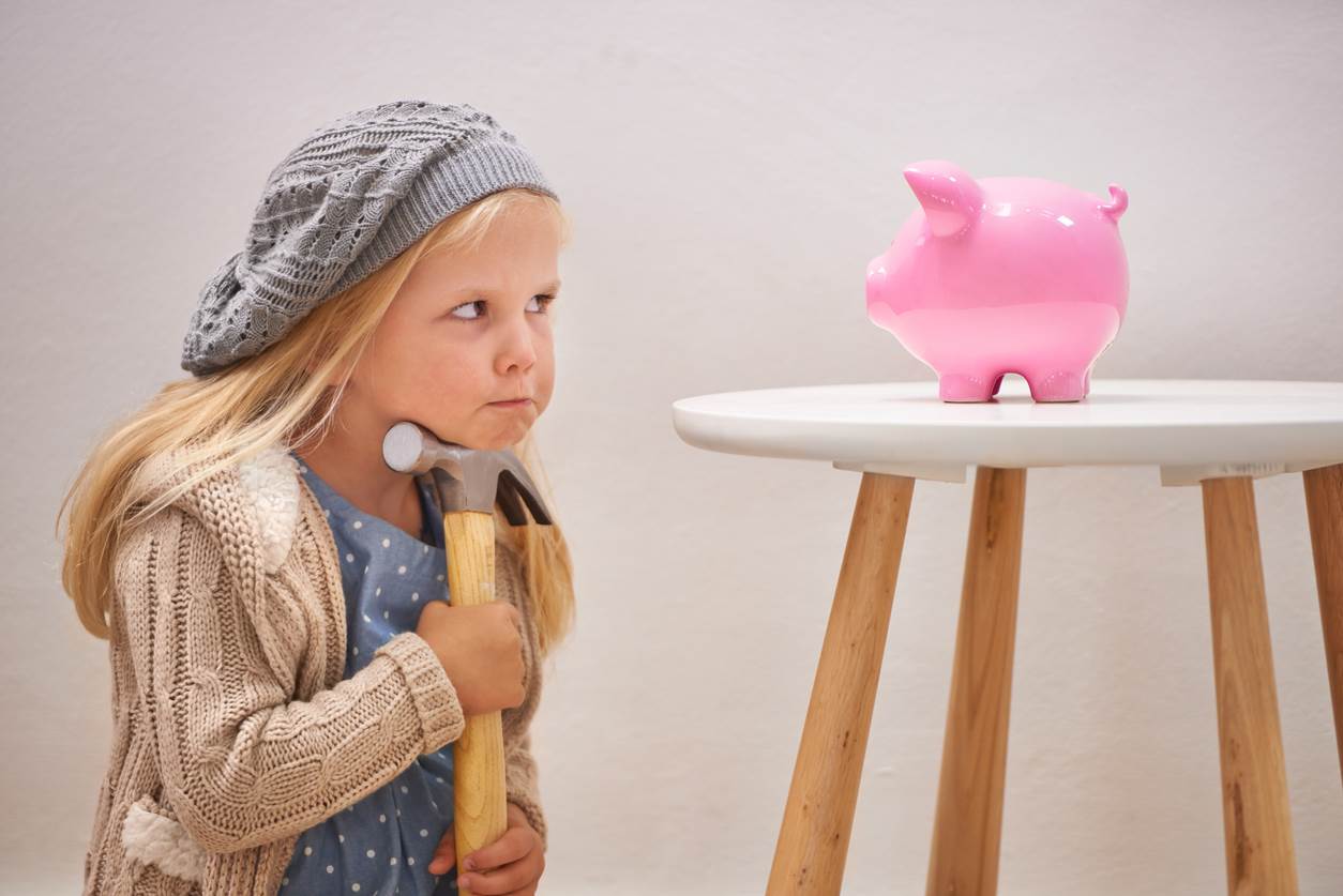 Cute girl with a hammer looking at a piggy bank