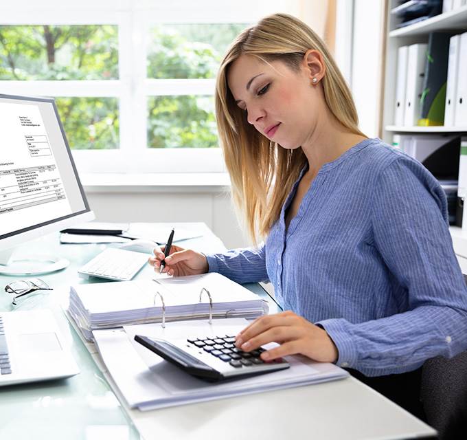 A woman working at a desk with papers and multiple computers