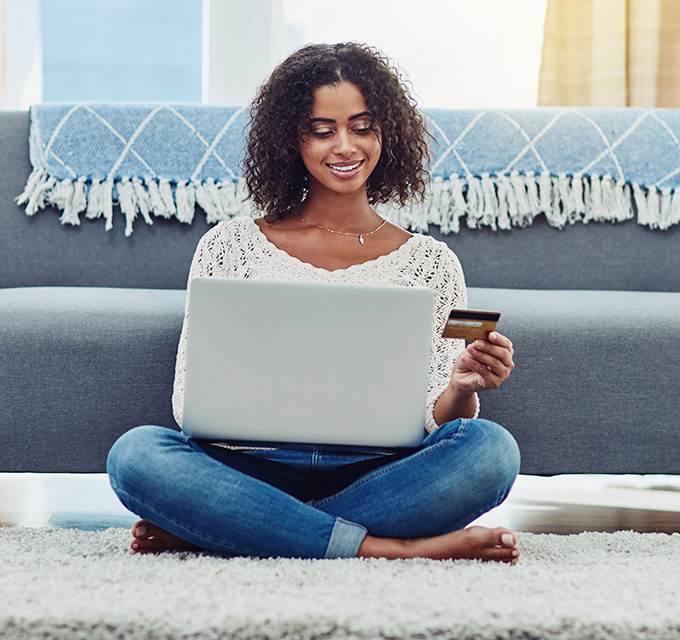 A woman sitting on the floor with a laptop and credit card